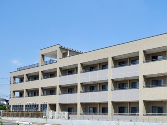 天気が良い日にプリエライフ狭山を写した写真。マンション風の鉄骨造の建物
