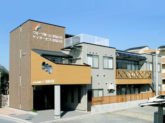 ブラウン系の２階建ての建物。２階部分にはベランダが付き、屋外階段も設置されている。