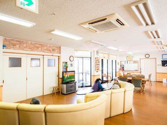 黄色いソファが置かれたフローリングの共有スペースには大きなテーブルセットやテレビが置かれている。