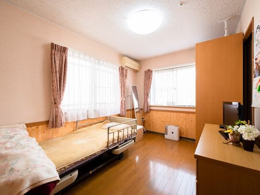 寝具付きのベッドやタンス、テレビなどが置かれた部屋にはカーテンが付いた大きな窓が二つ付いている。