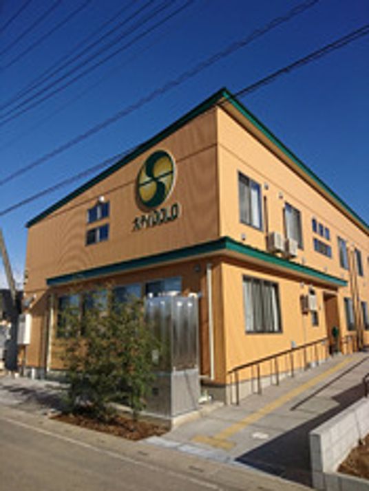 ２階建ての建物は玄関前に手すり付きのスロープが付いている。草木も植えられている。