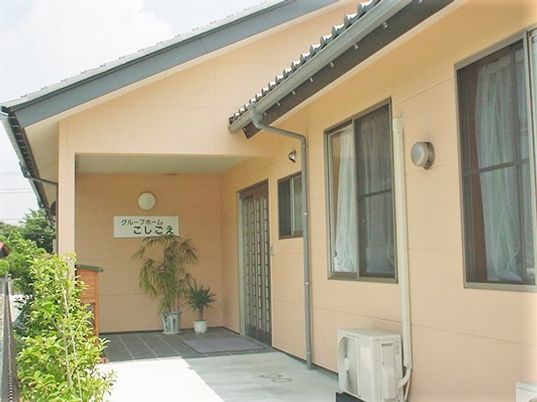 一軒家の入り口のような施設エントランス。施設名が掲げられた看板、観葉植物などがある