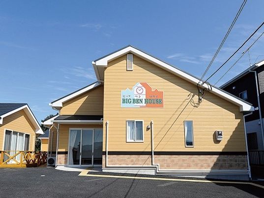 ベージュの外壁には住宅名とイラストが描かれ、玄関まで点字ブロックが敷かれている。