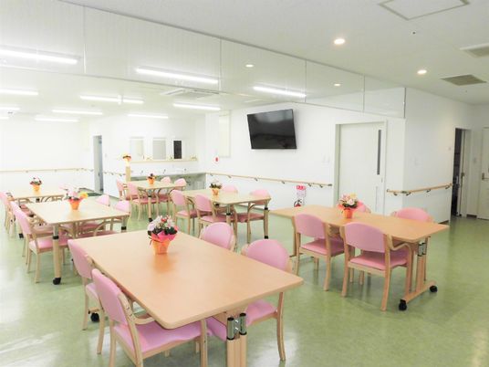 四人掛けのテーブルと椅子が複数組並んでいる食堂のような場所。大きなテレビが右奥の壁に掛けられている