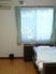 フローリングの部屋には寝具付きのベッドやゴミ箱、エアコンがあり、窓にはレースカーテンとカーテンが付いている。