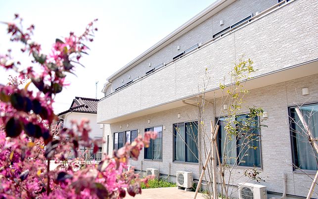 ２階建ての建物は日当たりのいい場所に建っている。外壁はベージュで2階部分にはベランダが付いている。