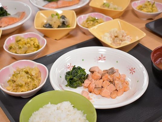 一口サイズにカットされた鮭やホウレン草が盛られたメインの皿を中心に副菜や白いご飯、汁物が置かれている。