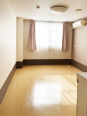 フローリングの居室にはエアコンと照明、カーテンが付いた大きな窓がある。家具は置かれていない。