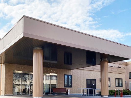 2階建ての建物はブラウン系で大きな車寄せが玄関につき、ベンチや手すり付きのスロープなどもも設置されている。