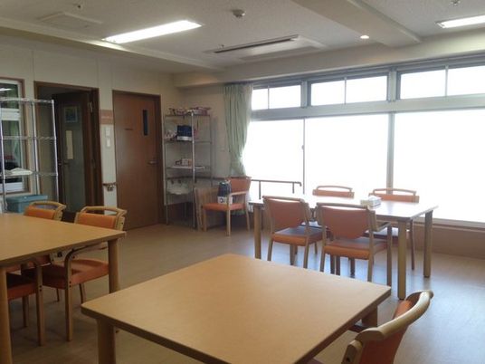 木製の4人掛けのダイニングテーブルセットが複数置かれた食堂にはカーテンが付いた大きな窓がある。