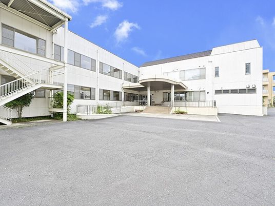 白を基調とした２階建ての建物は日当たり良好で玄関には緩やかなスロープと階段が設置され、広い駐車場もある。