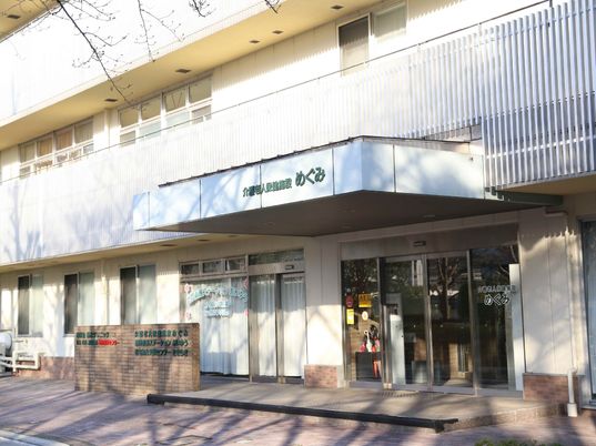 寝具付きのベッドや大きなテレビ、テーブルセットなどがあるフローリングの部屋には車いす対応のキッチンや冷蔵庫もある。