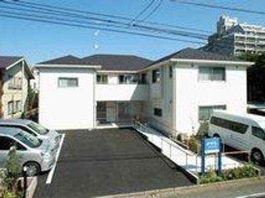 2階建ての建物は白い外壁にグレーの屋根。広い駐車場もついている。