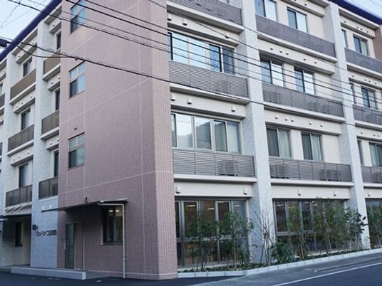 ブラウン系の建物の玄関には緩やかなスロープがあり、建物の周りには草木が植えられている。