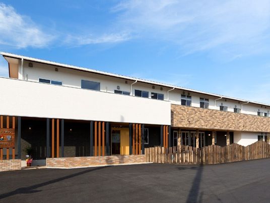 2階建ての建物は横に長く、2階部分にはベランダが付き、広い駐車場が設置され、日当たりのいい場所に建っている。