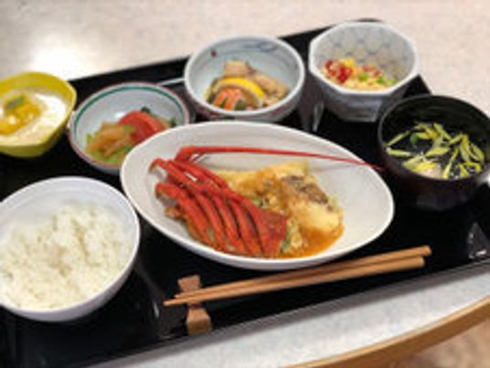 カニ料理をメインに、白いご飯やたくさんの小鉢が並んだ黒いトレー。箸置きには木製の箸が置かれている。