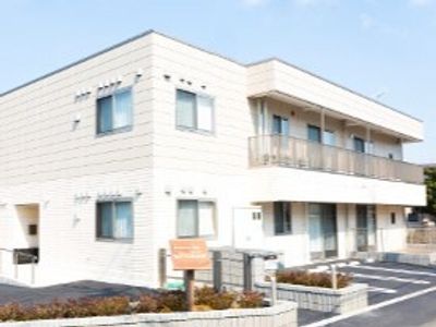 白を基調とした２階建ての建物は日当たり良好で建物の前には駐車場などがあり、2階部分にはベランダも付いている。