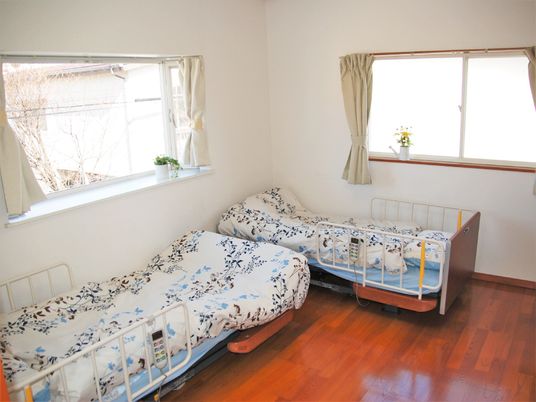 ベッドが二るL字型に並んでいる二人部屋の様子。窓が２面にある明るい部屋