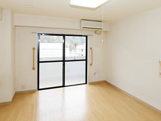 フローリングの居室には家具はなく、エアコンと緊急通報装置があり、大きな窓がある。