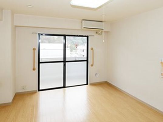 フローリングの居室には家具はなく、エアコンと緊急通報装置があり、大きな窓がある。