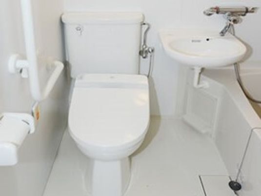 エル字型の手すりやオレンジの呼び出しボタンが付いたトイレには浴槽もある。全体的に白でまとめられている。