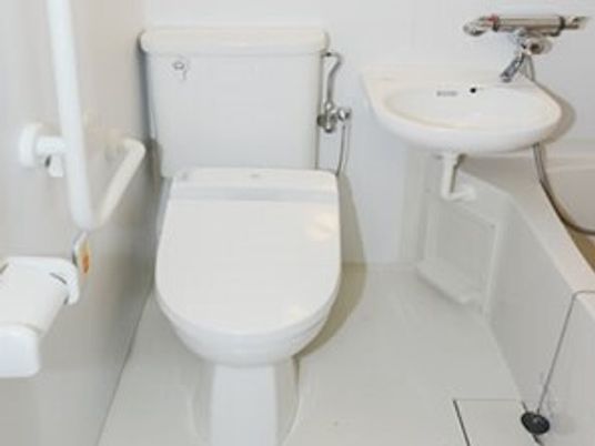 エル字型の手すりやオレンジの呼び出しボタンが付いたトイレには浴槽もある。全体的に白でまとめられている。