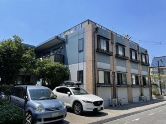 日当たりのいい場所に建って2階建ての建物。敷地内には駐車場も完備され、木も植えられている。