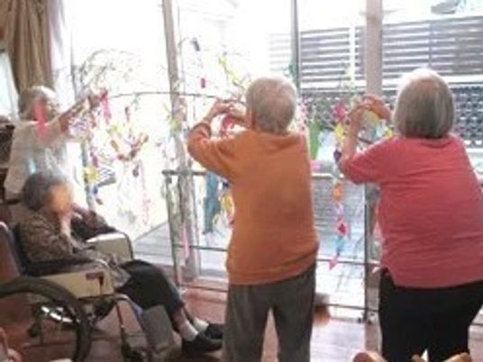 施設内で飾りつけをしている様子。複数名が笹の葉っぱに何かを取り付けている様子が分かる