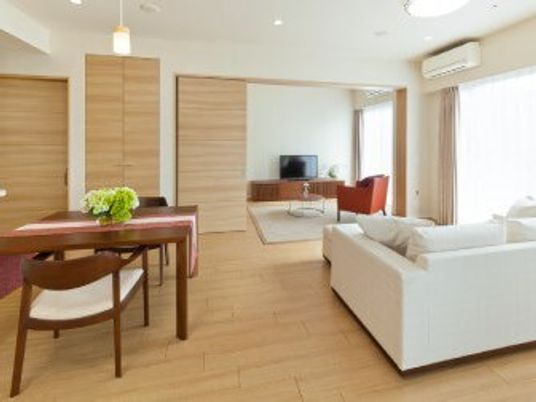 エアコンや複数名用ソファ、テレビ、ダイニングテーブルが整った居室の様子