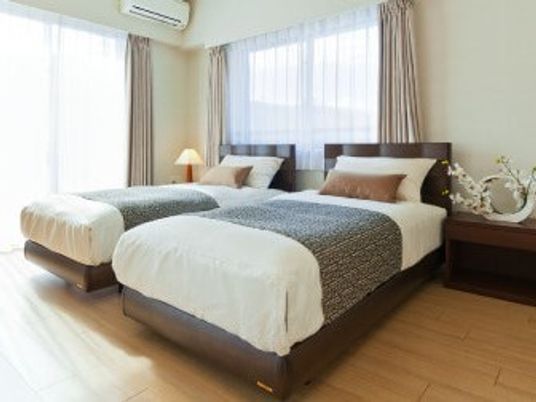 ベッドが二つ並んでいる寝室の様子。明るい窓が付いている寝室の写真