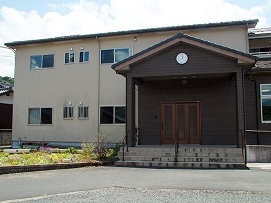 白い壁と学校のような入り口が印象的な建物。木造２階建ての建物の様子
