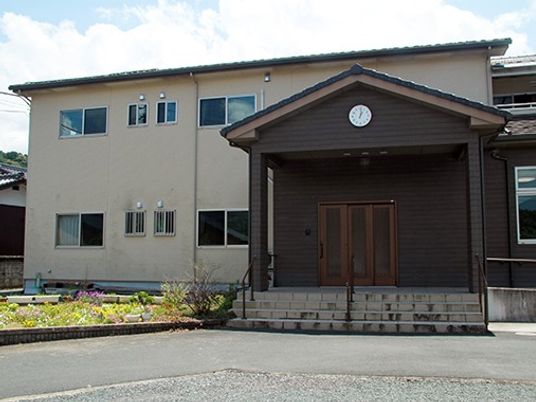 白い壁と学校のような入り口が印象的な建物。木造２階建ての建物の様子