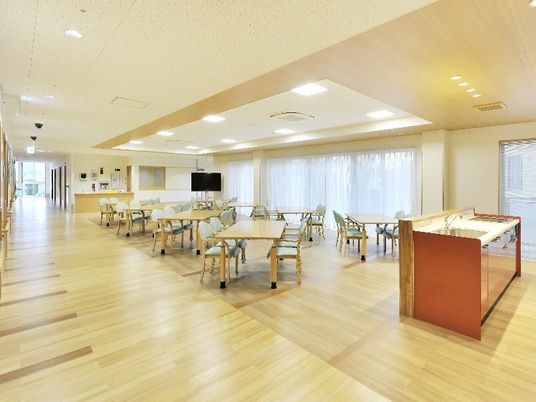 木製のダイニングテーブルが並び、いすがセットされた食堂。明るい雰囲気で窓も大きい。