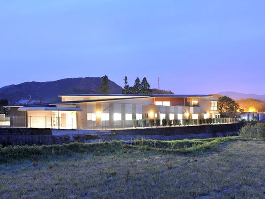 自然に囲まれた2階建ての建物。夕暮れ時になり、館内の灯りが漏れている。