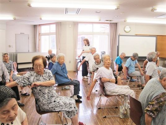 高齢者が椅子に座ってストレッチしている様子。施設内のrレクリエーションの様子