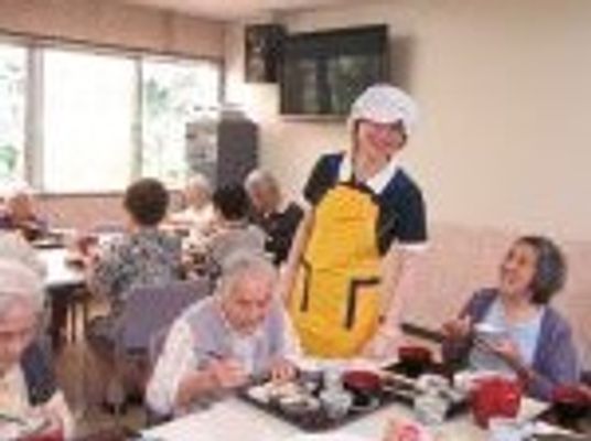 スタッフと高齢者が談笑しながら食事を楽しんでいる様子。施設の一場面の写真