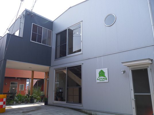 ２階建ての建物の側面に出入り口がある。敷地内には木や花を育てるスペースもある。