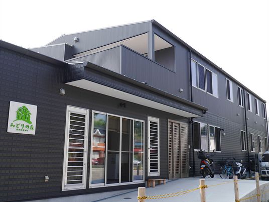 黒を基調とした２階建ての建物。敷地内にはバイクや車が止められている。