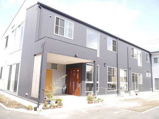 ２階建ての建物は黒と白の２色使い。玄関周りには季節の花や木が植えられている。