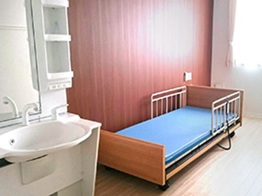 介護ベッドが置かれたフローリングの部屋には大きな窓があり、車いす対応の洗面所が設置されている。