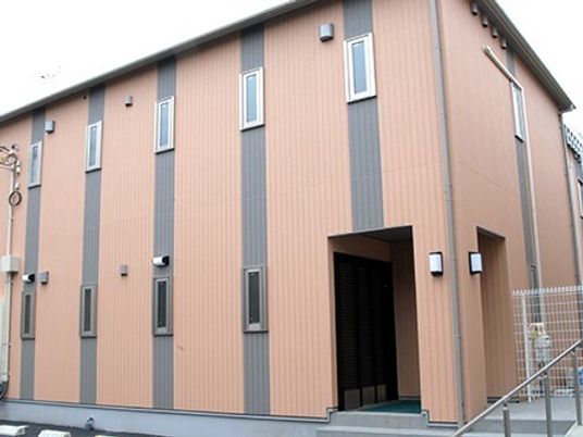 ブラウン系の２階建ての建物は日当たり良好で手すり付きのスロープや階段が玄関にある。