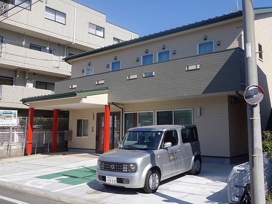 赤い柱が印象的な玄関には車寄せが付き、建物にはベランダもある。