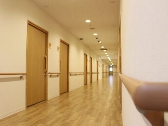 手すりがついている施設内の廊下の様子。個室のドアが並んでいる