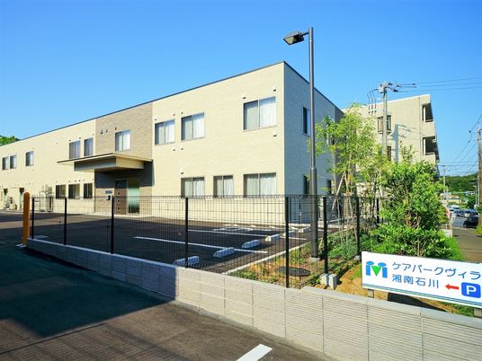 ベージュを基調とした2階建ての建物の外壁にはブラウンのアクセントもあり、駐車場も付いている。