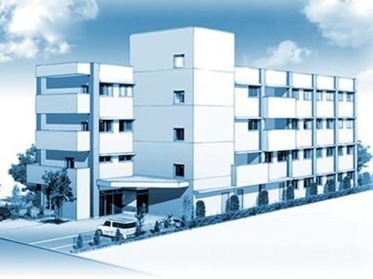 4階建ての建物は白を基調としていて、周辺には駐車場があり、緑があふれている。
