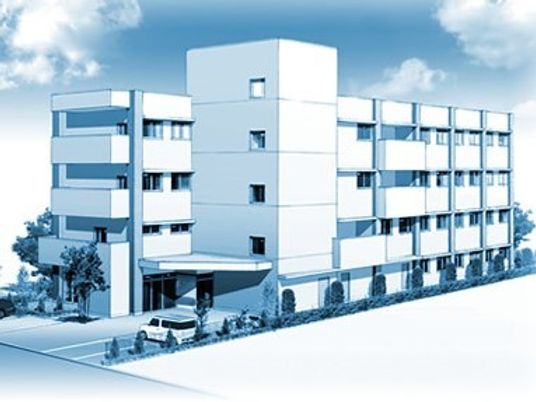 4階建ての建物は白を基調としていて、周辺には駐車場があり、緑があふれている。