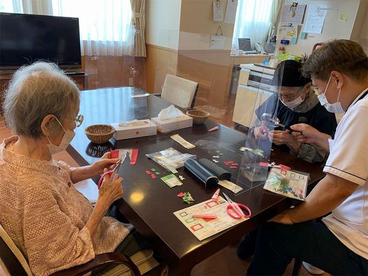 テーブルの上にはたくさんの色紙があり、高齢女性たちが真剣な表情で創作活動をしている。