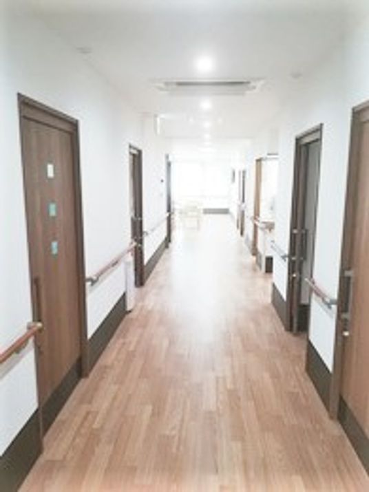 まっすぐな廊下は白い壁に木製の手すりが付き、居室は引き戸となっている。