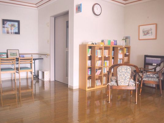たくさんの本が並んだ本棚の前には一人用の椅子が2脚置かれ、左側のトイレの前にはテーブルセットが置かれている。