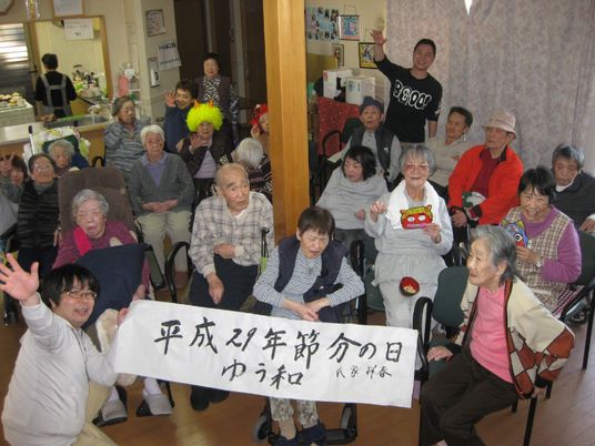 節分の垂れ幕を前に、鬼の面やかつらをかぶった人たちもいる集合写真。